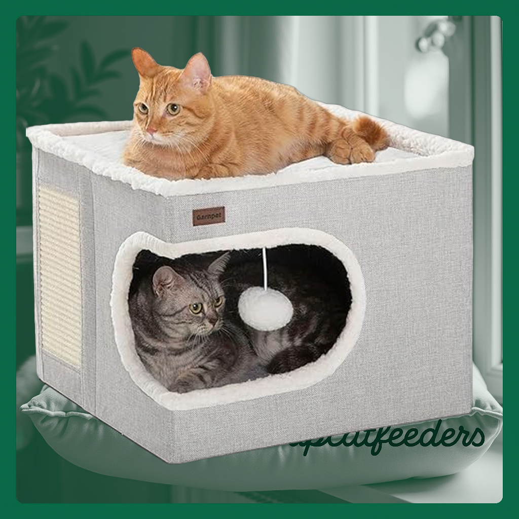A grey, cave-style cat bed fitted with playful toys, a scratch pad, and a machine-washable cushion